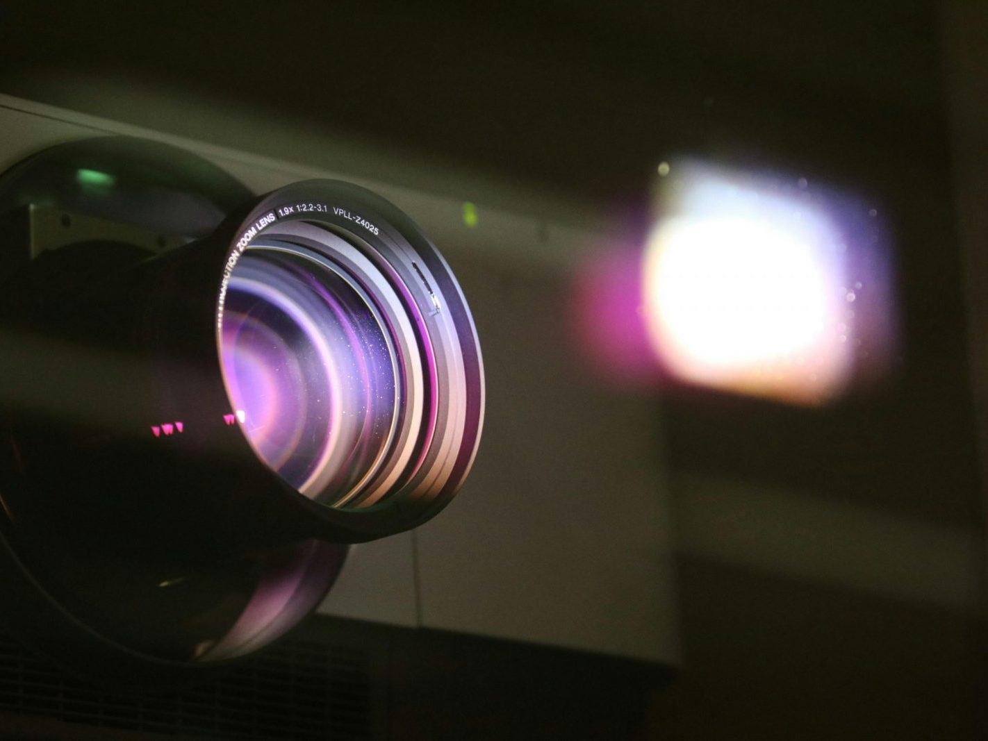 Close-up view of a projector lens with light reflections, highlighting optics and technology.
